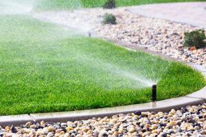 Lawn sprinkler watering a green, well-kept lawn with a pebble border.